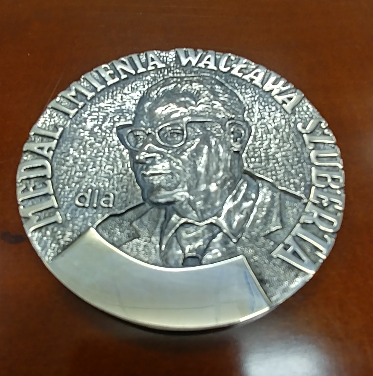 Srebrny medal z twarzą mężczyzny w okularach otoczony napisem Medal Wacława Szuberta