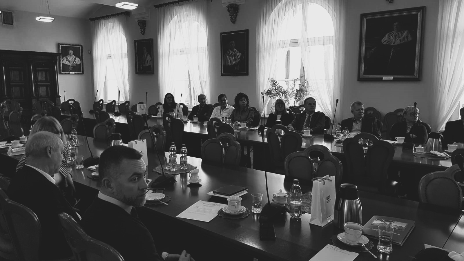 Kilkanaście osób siedzi przy długich stołach konferencyjnych